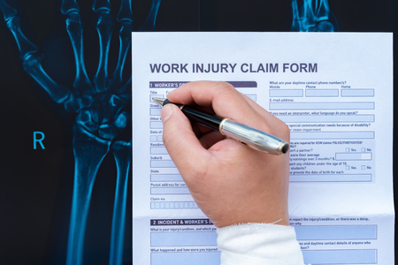 filling up a work injury claim form with a wrapped hand on top of an X-ray film medical and insurance conceptの写真素材