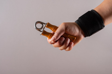 hand with a wrist protective strap doing exercises by squeezing an A shape hand trainerの写真素材