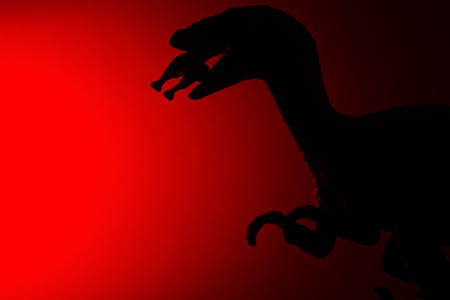 shadow of Deinonychus biting a smaller dinosaur with red light in darkの写真素材