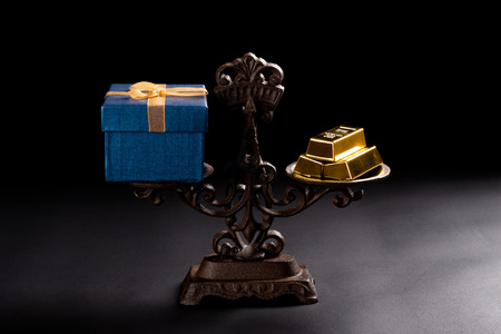 present box and gold bars on a balanced scale concept of expensive gifts
