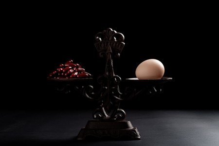 dozens of capsules and an egg on a balanced scale concept of healthy eating and alternative lifestyleの写真素材