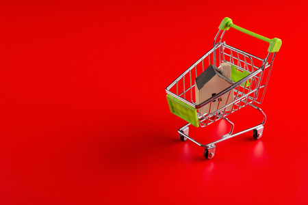 A house model in a shopping cart on red backgroundの写真素材