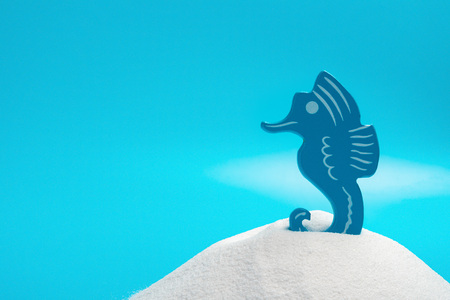 toy seahorse on white sand on blue background concept of summer vacationsの写真素材