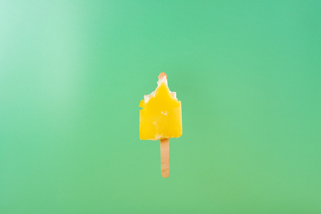 half eaten yellow ice cream stick on a light green background
