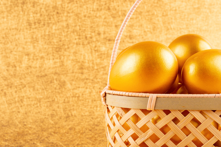 gold eggs in a basket on golden background with copy spaceの写真素材