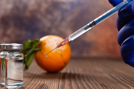 medical syringe and bottles of vaccine with a moldy orange on backgroundの写真素材