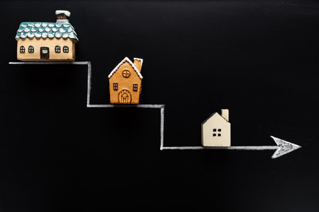 going down arrow with samller and smaller houses on blackboard backgroundの写真素材