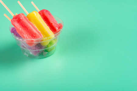 colorful ice cream stick melting in a cup on light green with copy space