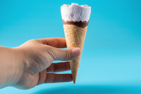 hand holding a peanut ice cream cone on blue background