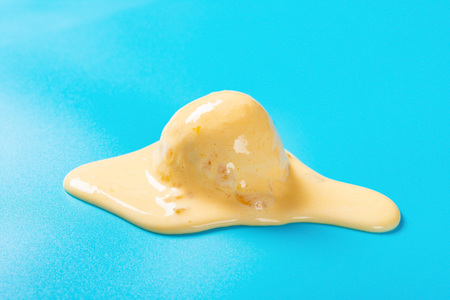 side view mango flavor ice cream ball in a melting process on blue backgroundの写真素材