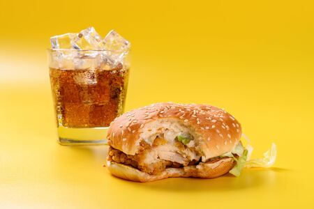 hamburger with a bite and cup of iced cola on a yellow backgroundの写真素材