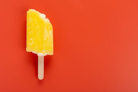 yellow ice pop with a couple of bites on an orange backgroundの写真素材