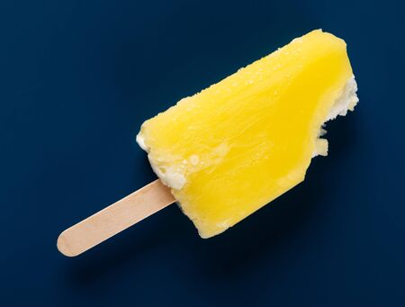 yellow ice cream stick with some bites on a dark blue backgroundの写真素材