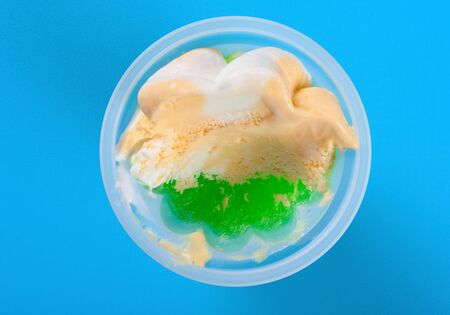 top view cup of orange and green color ice cream with some bites on blue backgroundの写真素材