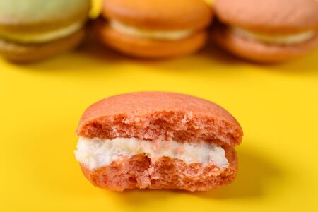 half eaten pink macaroon on yellow with some macaroon on backの写真素材