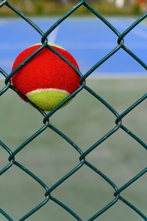 tennis ball stuck on the wire fence of a outdoor court vertical compositionの写真素材