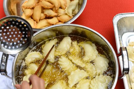 lady deep frying traditional Chinese Yau Kok Zai or sweet dumpling with some raw ones nearby for...