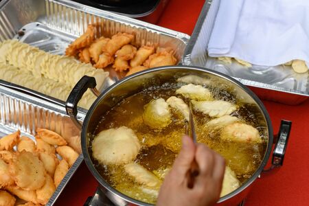 lady deep frying traditional Chinese Yau Kok Zai or sweet dumpling with some raw ones nearby for...