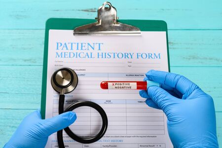 doctor holding a blood test tube with positive result and the patient history form the X on positive contains can be removedの写真素材