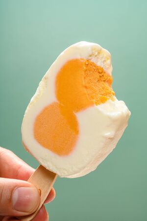 hand holding egg shape ice cream stick with a bite on green background