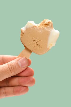 hand holding a half eaten cheese and lemon flavor ice pop on green background