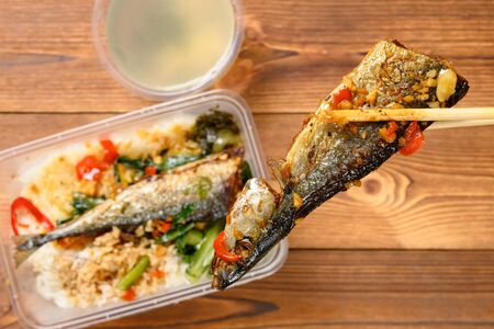 chopsticks taking out piece of fried fish from box of fast food