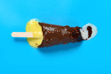 top view vanilla flavor with chocolate and peanuts outer ice cream stick starts melting on a blue...