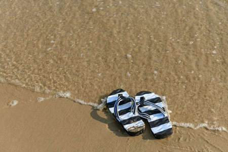 pair of slippers in front of a beach with wave coming