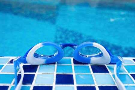 blue swimming goggles on the edge of a swimming poolの写真素材