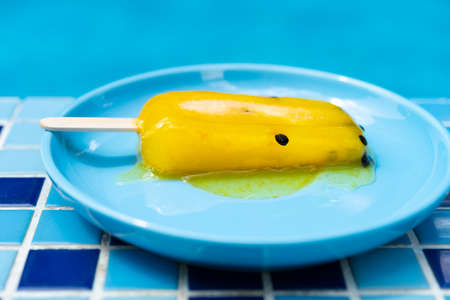 a passion fruit icde pop in a melting process in front of a swimming poolの写真素材
