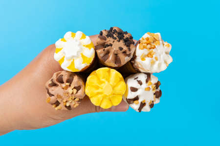 top view mans hand holding six mini size ice cream cones with different flavors on blue