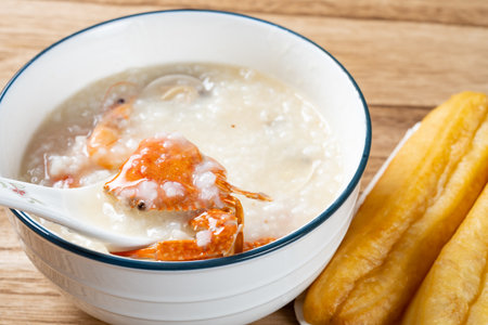 spoon taking out crab from seafood porridge with deep-fried dough sticks nearbyの写真素材