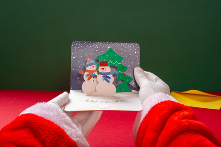 Santa Claus holding a 3D gift card with snowmen and fir-treesの写真素材