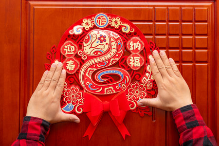 man sticking a Chinese New Year of the Snake decoration to a door at horizontal composition translation of the Chinese characters are Welcoming Spring and Embracing Fortune no logo no trademarkの写真素材