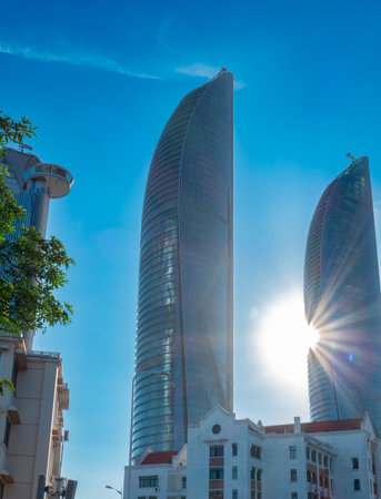 two sleek and curved skyscrapers gleam under the low sun, towering above a mix of old city buildings and greenery in a vibrant urban skylineの写真素材