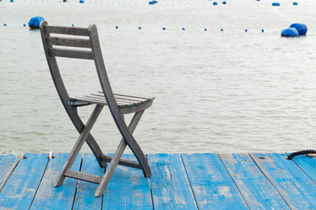 a solitary wooden chair rests on a blue dock and gazing out over calm sea at horizontal compositionの写真素材