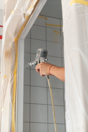 a person carefully spray-paints the interior of a tiled space, with protective coverings ensuring a clean and precise finishの写真素材