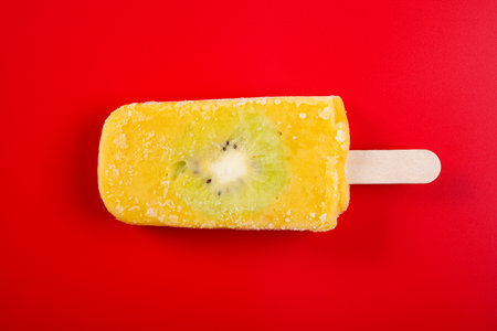 fresh mango and milk flavor popsicle with slice of kiwi fruit on red backgroundの写真素材