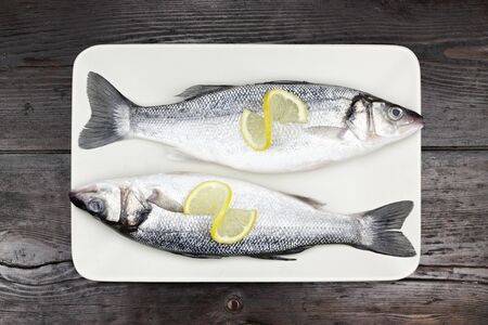 Fresh sea bass in a white plate, on a wooden surface.の写真素材