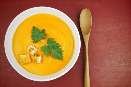 Close up of a bowl of carrot soup on red surface の写真素材