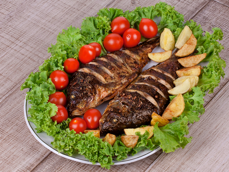 Whole grilled fish carp served with potatoes, tomatoes cherry and saladの写真素材