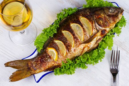 Whole grilled fish carp served with salad and lemon; glass of wineの写真素材
