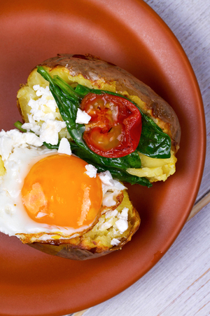 Baked potato with fried egg, feta, spinach and tomato cherryの写真素材