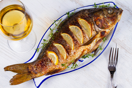Whole grilled fish carp served with salad and lemon; glass of wineの写真素材