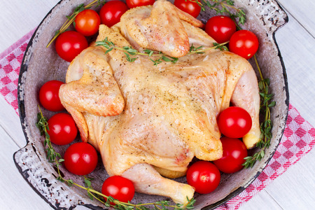 Whole fresh raw chicken prepared for roast with thyme and tomatoes cherryの写真素材