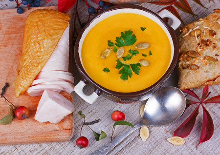 Bowl of pumpkin soup,  whole pumpkin, smoked chicken, bread and red leaves on autumn backgroundの写真素材