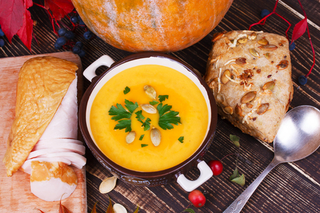 Bowl of pumpkin soup,  whole pumpkin, smoked chicken, bread and red leaves on autumn backgroundの写真素材