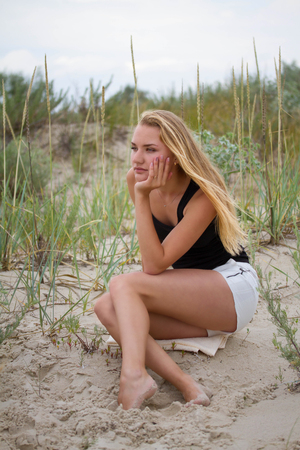 Outdoor portrait of melancholy and sad young pretty woman sitting on the sand near the sea aloneの写真素材