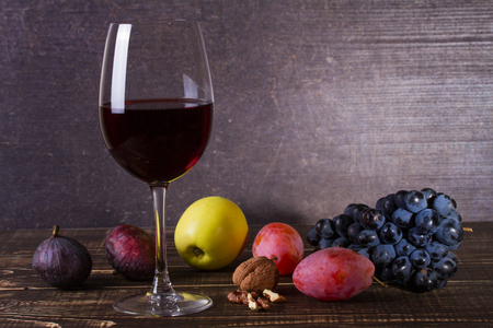 Glass of red wine, cheese, grape, walnuts, figs, plums and apple on wooden background. Still lifeの写真素材