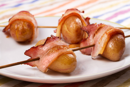 Bacon wrapped potato on skewers on white plateの写真素材
